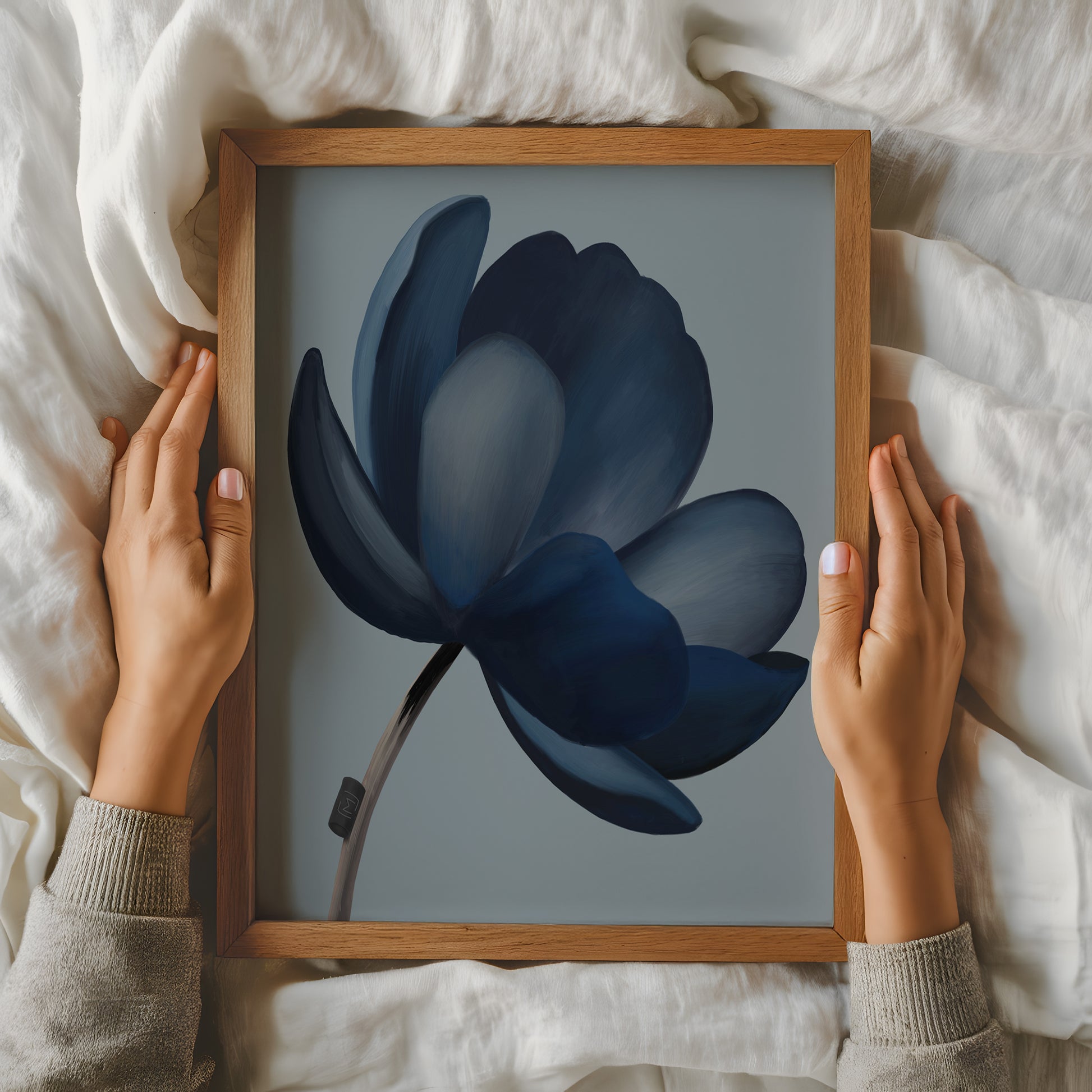 Håndmalet abstrakt blomst i støvede blå toner vist i ramme, holdt af hænder for at fremhæve størrelse og detaljer.